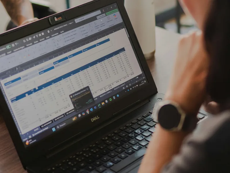 Ordinateur portable ouvert sur un tableur, une personne portant une montre connectée travaille à côté